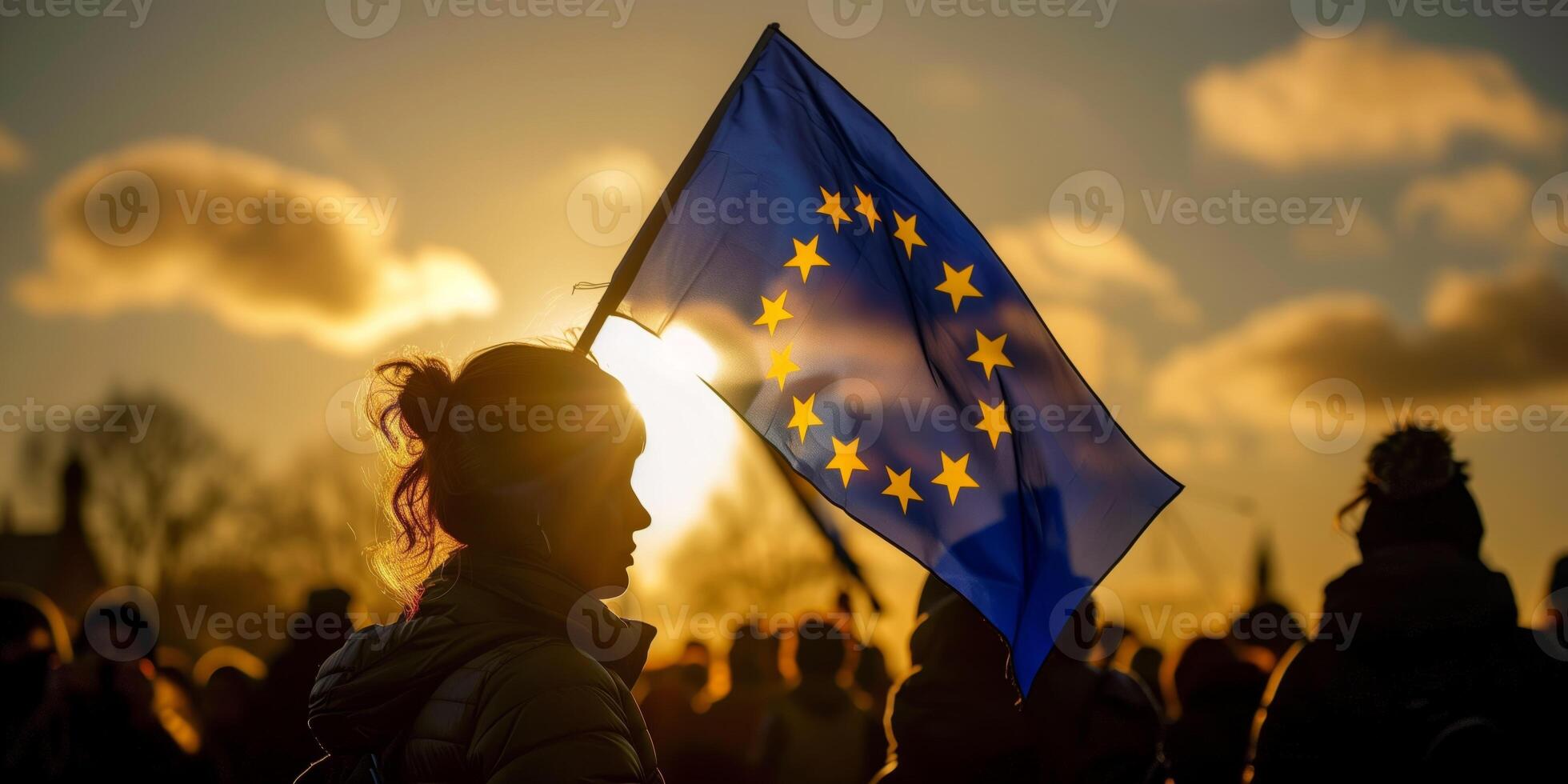 A silhouette of a woman holding a European Union flag during sunset with soft clouds and a crowd in the background photo
