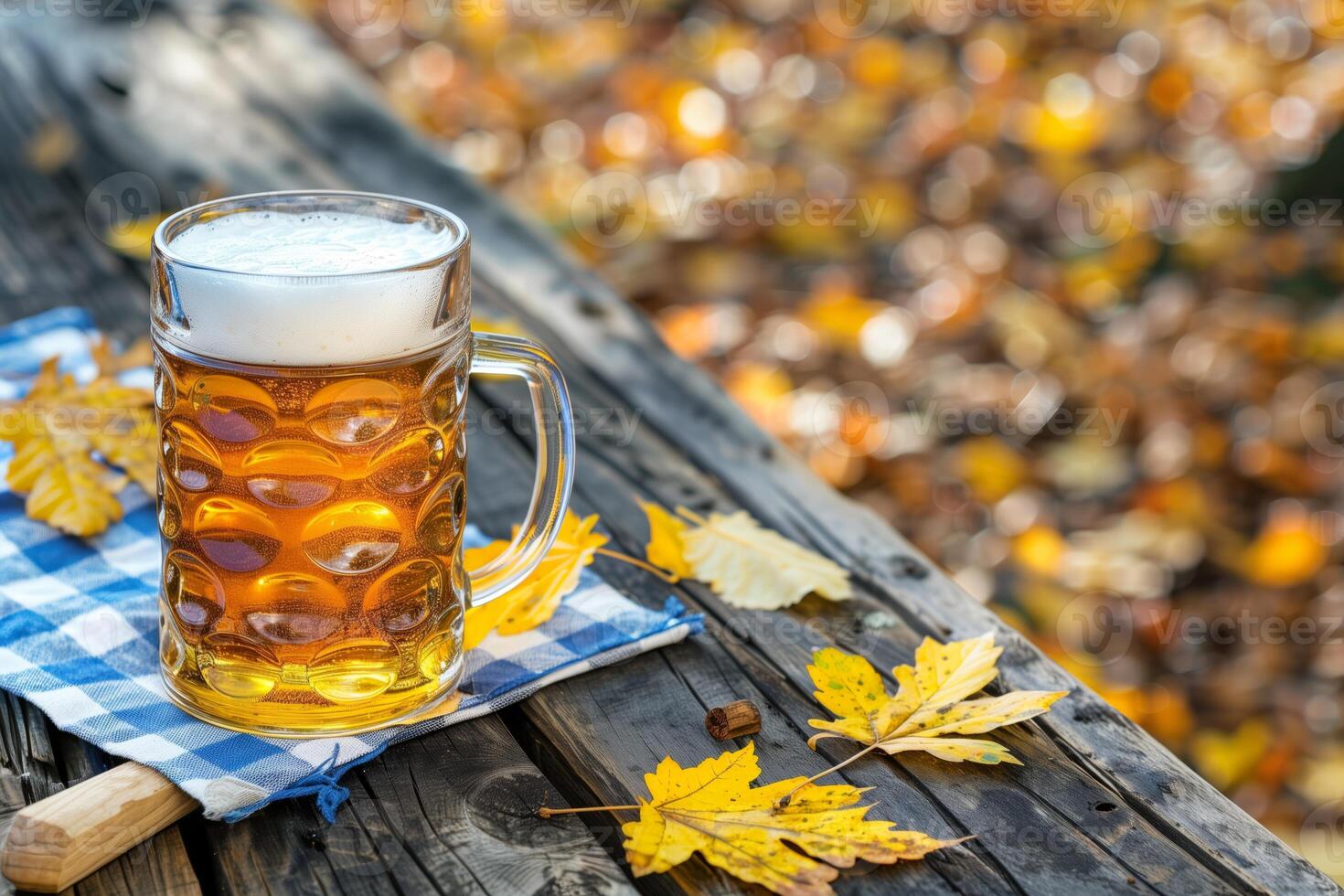 Glass of golden beer on a wooden table with autumn leaves and a blue checkered napkin outdoors photo