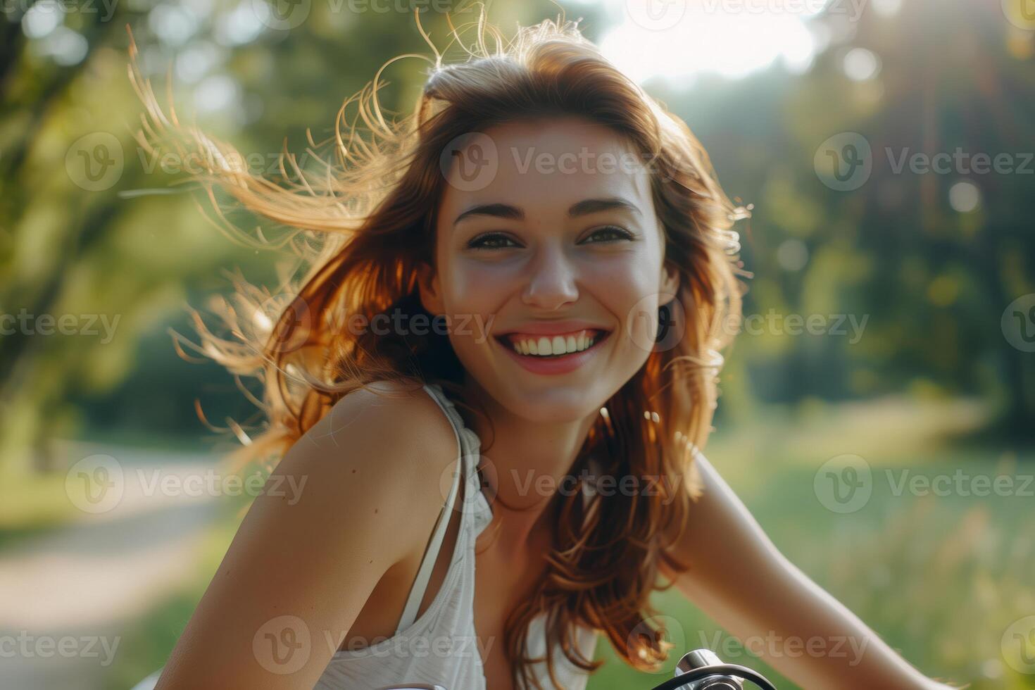 A happy young woman with flowing hair smiling outdoors, surrounded by lush greenery and soft sunlight, exuding natural beauty and joy photo