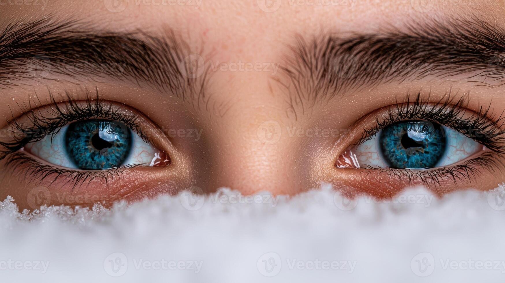 Close up of a womans blue eyes peering over a layer of snow photo