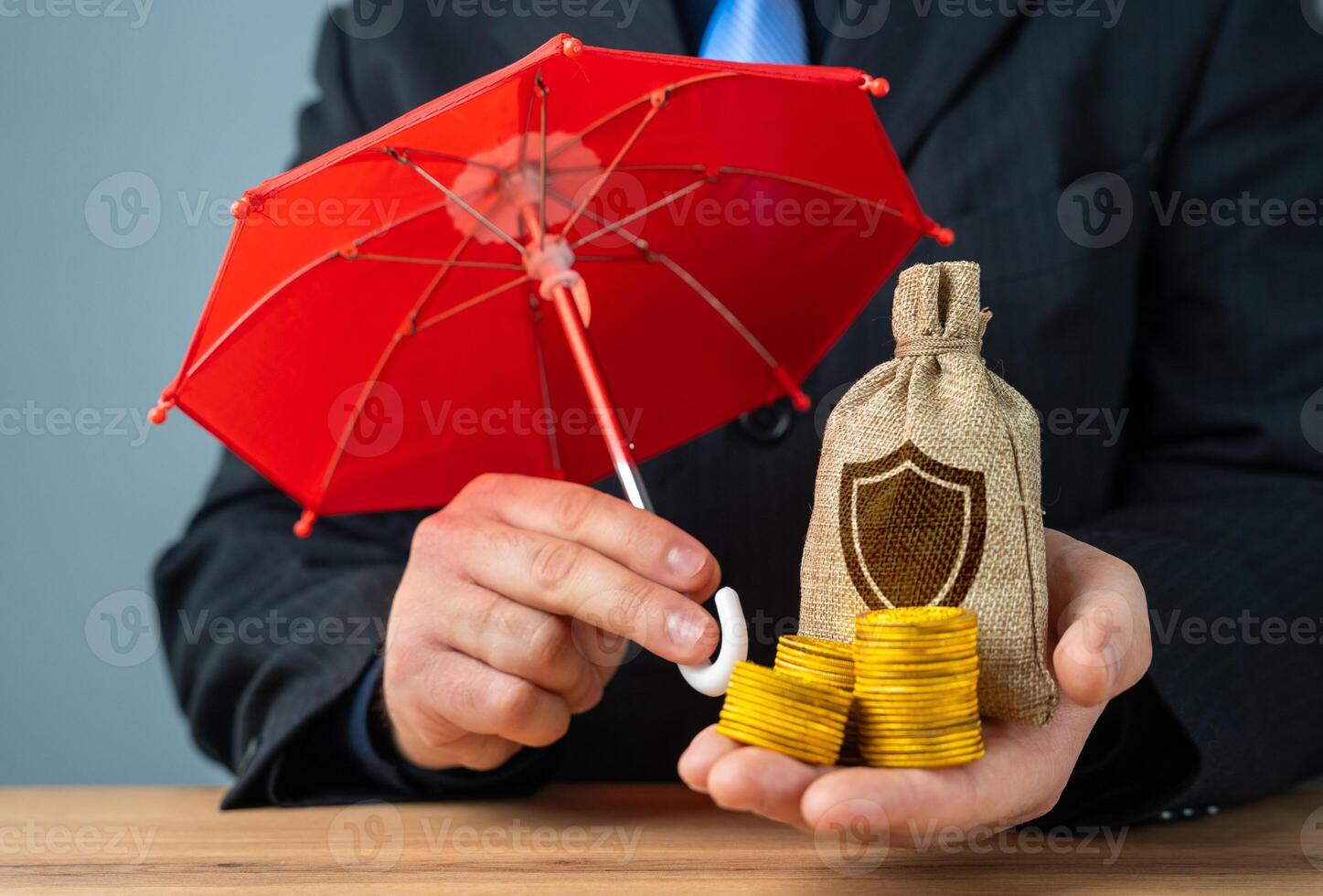 The businessman holds an umbrella over money. A bag with a shield symbol. Concept of protection and security. Cyber protection. Security budget. photo