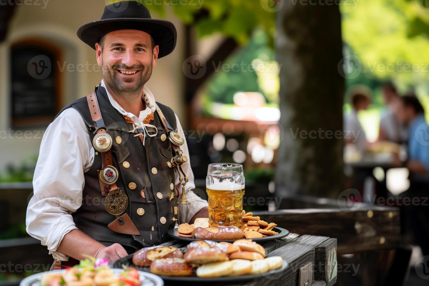 Smiling man in traditional Bavarian attire holding plates of pretzels and snacks with a beer stein in an outdoor beer garden setting photo