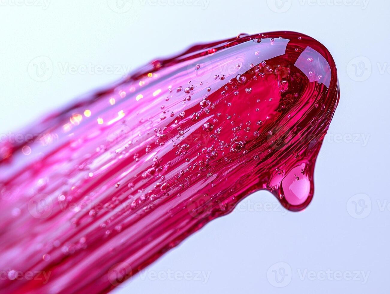 Clear pink lip gloss is captured mid drip from rounded applicator tip highlighting its glossy texture and dynamic movement against bright white background photo