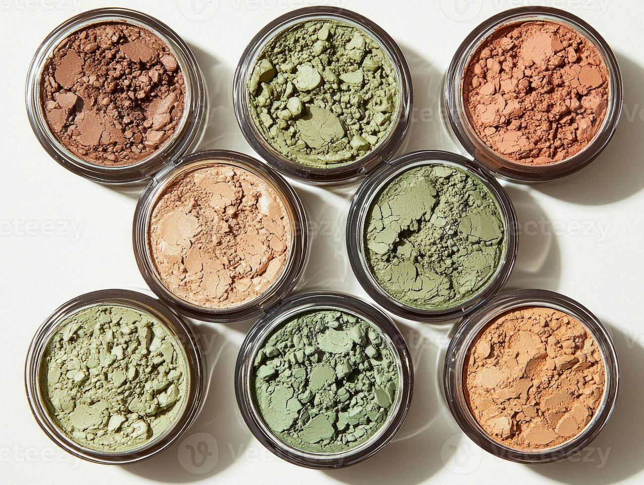 Cream eyeshadow pots are arranged showcase shades of champagne olive green and bronze. creamy textures reflect soft light against clean simple background photo