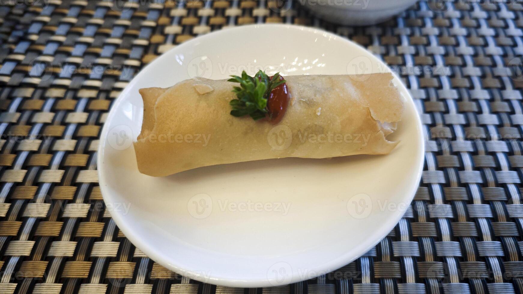 Crispy Spring Roll Garnished with Parsley and Chili Sauce on White Plate with Woven Table Mat Background photo