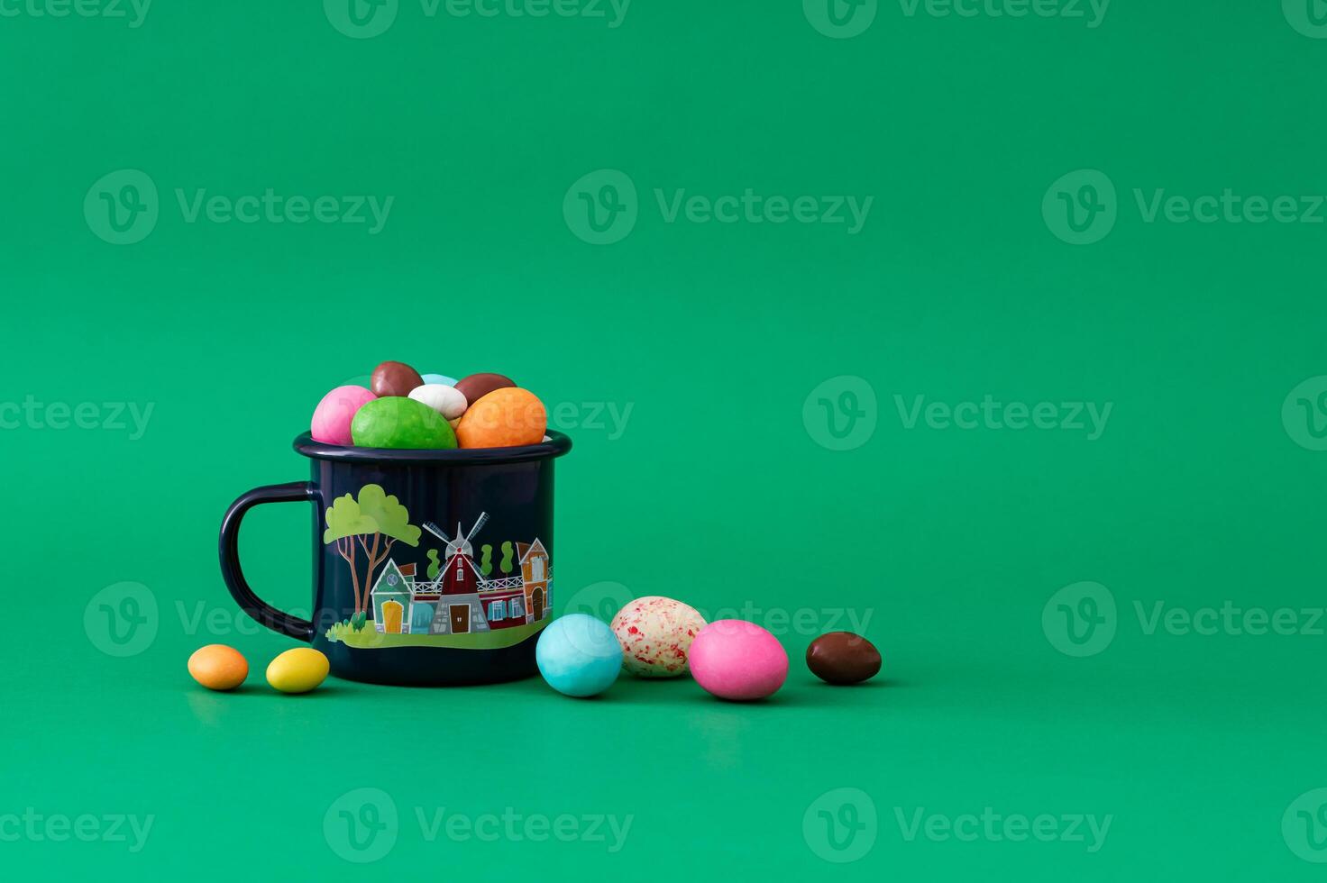 Colorful Easter chocolate eggs in enamel mug against green background. Minimal Easter concept. Creative festive spring holiday layout. Easter aesthetic. photo