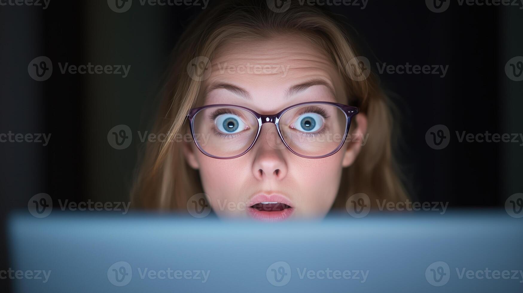 Surprised Woman with Glasses Looking at Computer Screen in Dark Environment, Expressive Close-Up with Emotional Reaction, Perfect for Technology, Lifestyle, and Cybersecurity Themes photo