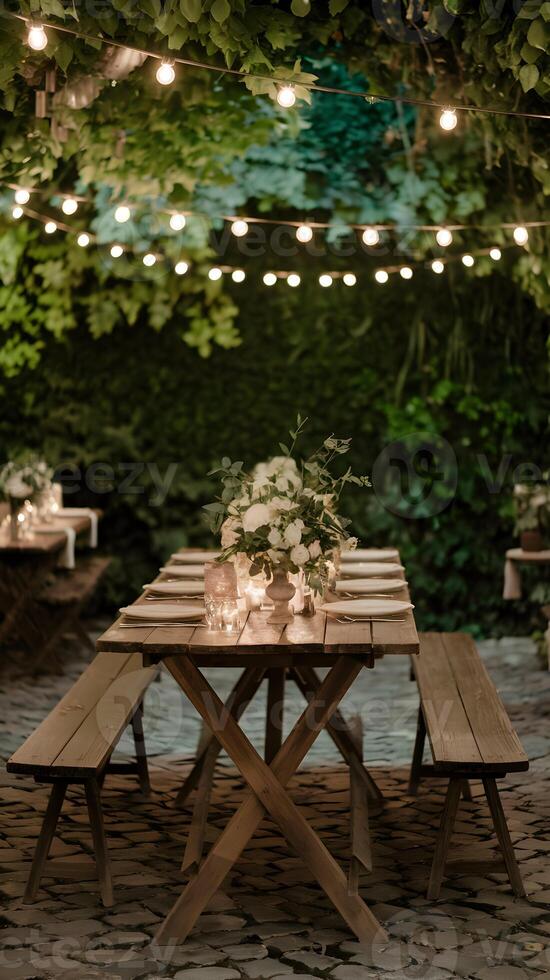 Rustic wooden table bathed in warm light, with green foliage and cozy string lights. Vertical Mobile Wallpaper photo
