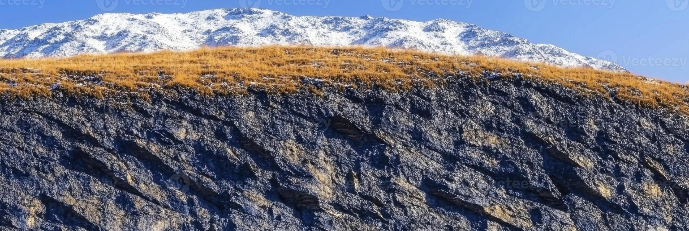 Rugged mountain landscape with snow-capped peaks and rocky cliffs under blue sky photo