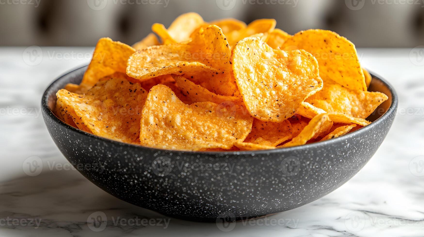 Tortilla chips rest in black ceramic bowl, displaying golden yellow corn texture with dramatic side lighting against white marble surface background. ceramic photo