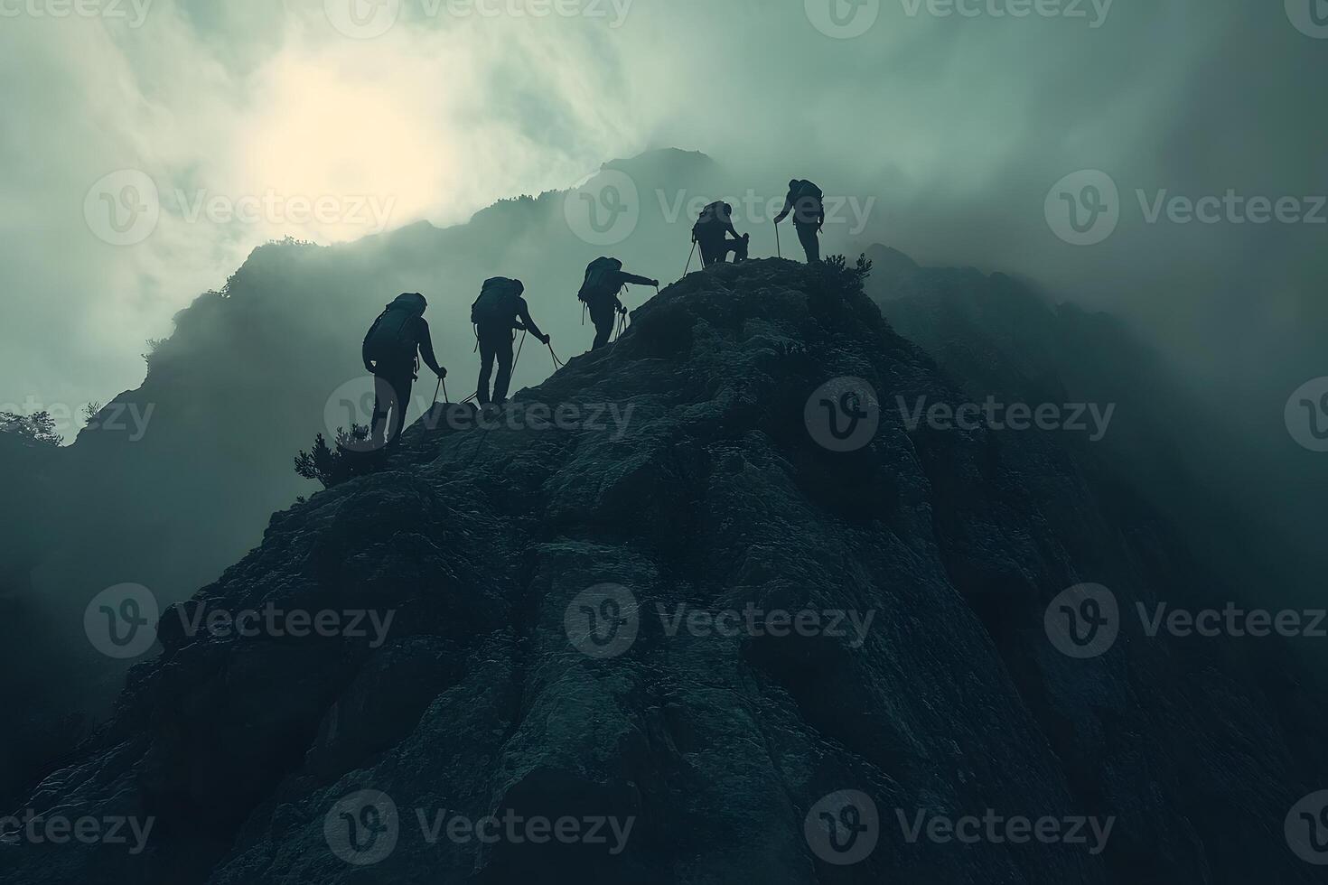 Silhouetted climbers ascend a misty mountain peak photo