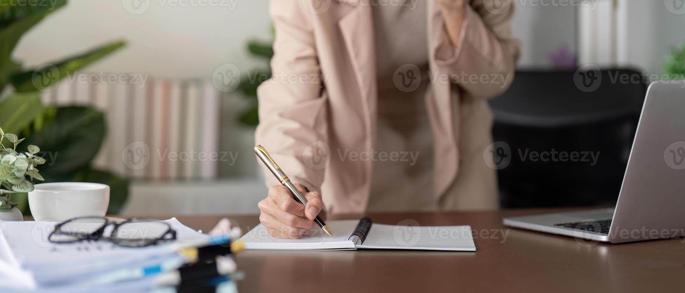 Focused businesswoman writing notes in a notebook while managing tasks in her modern office photo