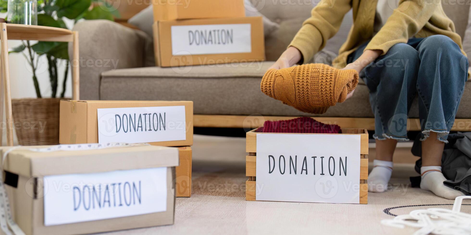 Woman placing warm knitted sweater into donation box, organizing clothes in a cozy living room photo