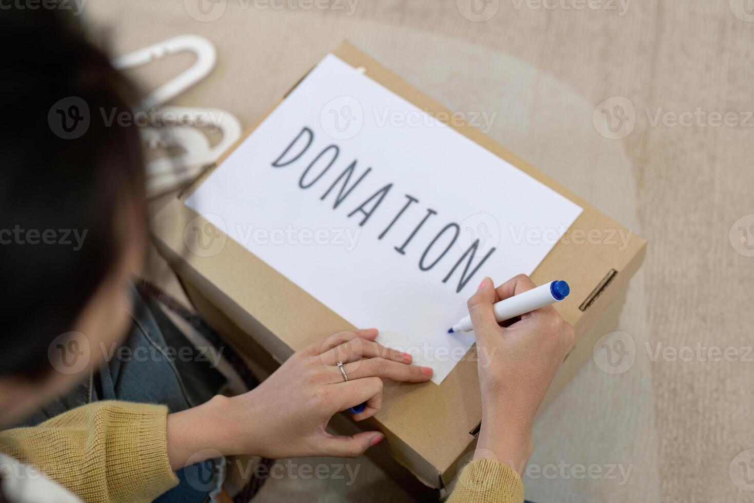 Close up of a woman labeling a donation box with marker, organizing clothes and hangers in a cozy living room photo