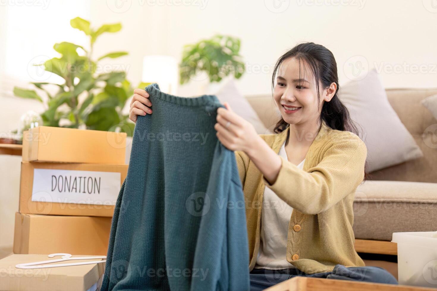 Joyful woman holding a sweater for donation in her cozy living room, organizing clothes for charitable purpose photo