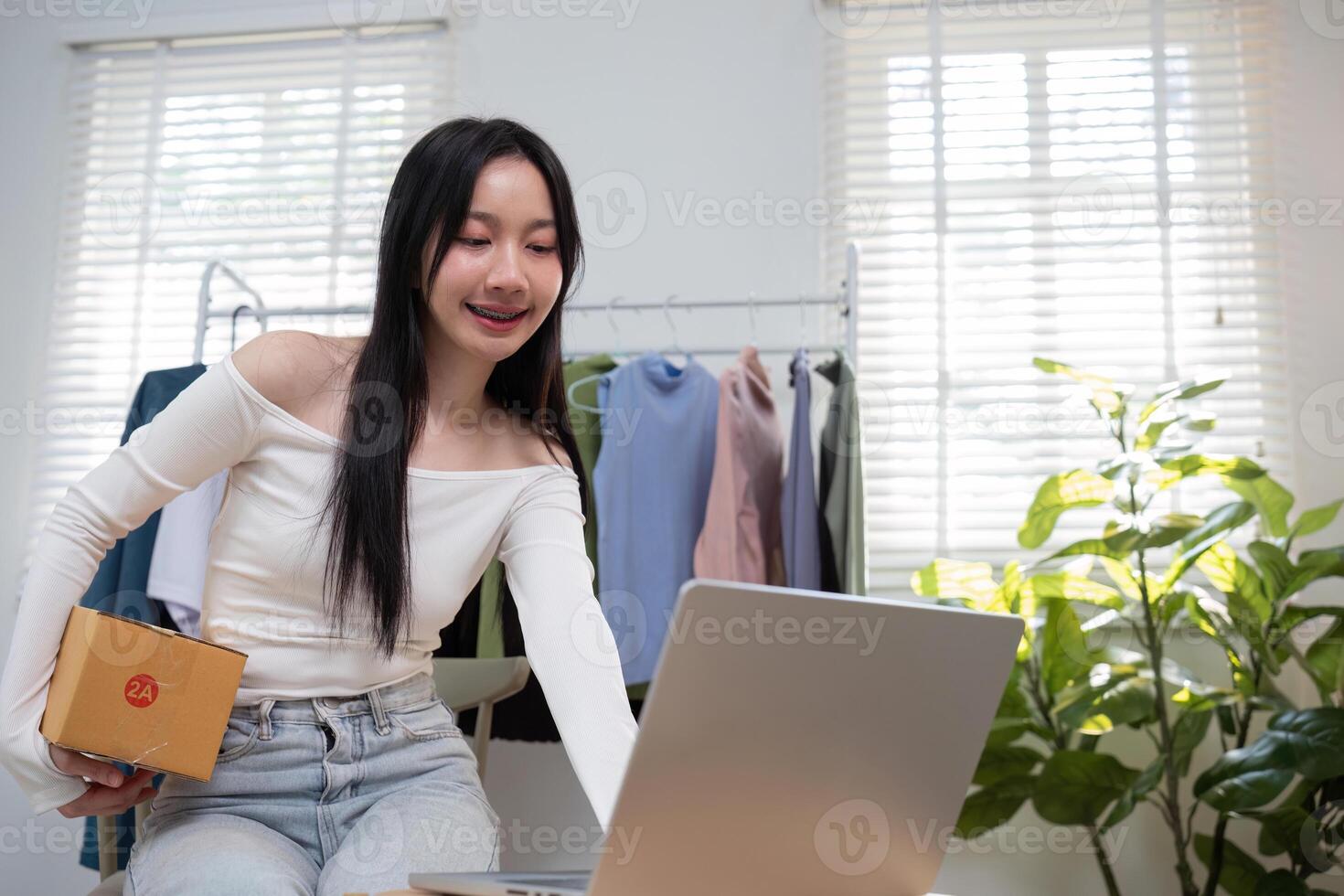 Excited young female entrepreneur preparing to ship an order while working on her laptop in her home clothing business photo