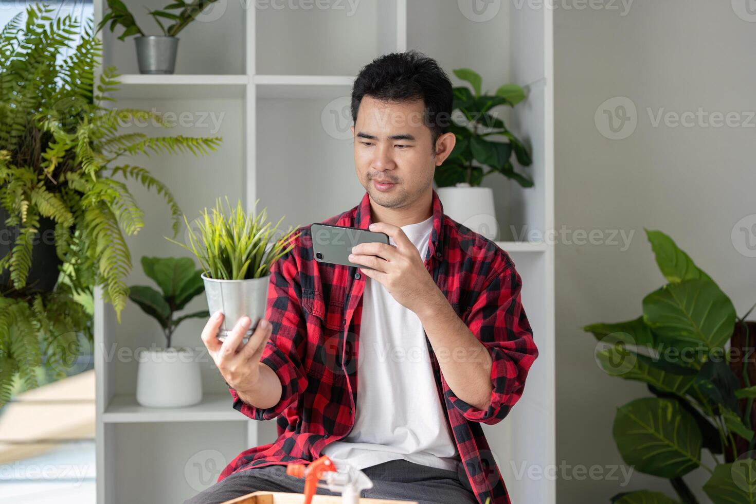Young man taking a photo of a potted plant with smartphone in a modern indoor garden
