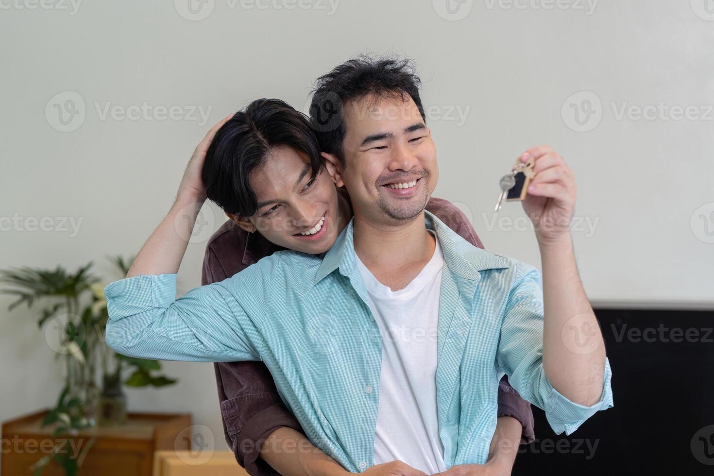 Happy gay couple holding house keys, celebrating their new beginning together with love photo