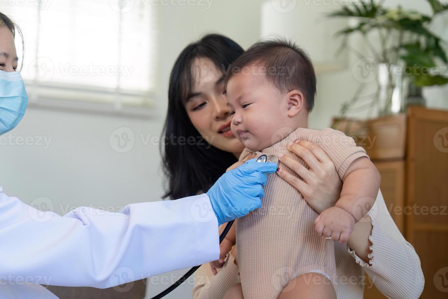Pediatrician checking baby's heartbeat as concerned mother looks on during health assessment photo