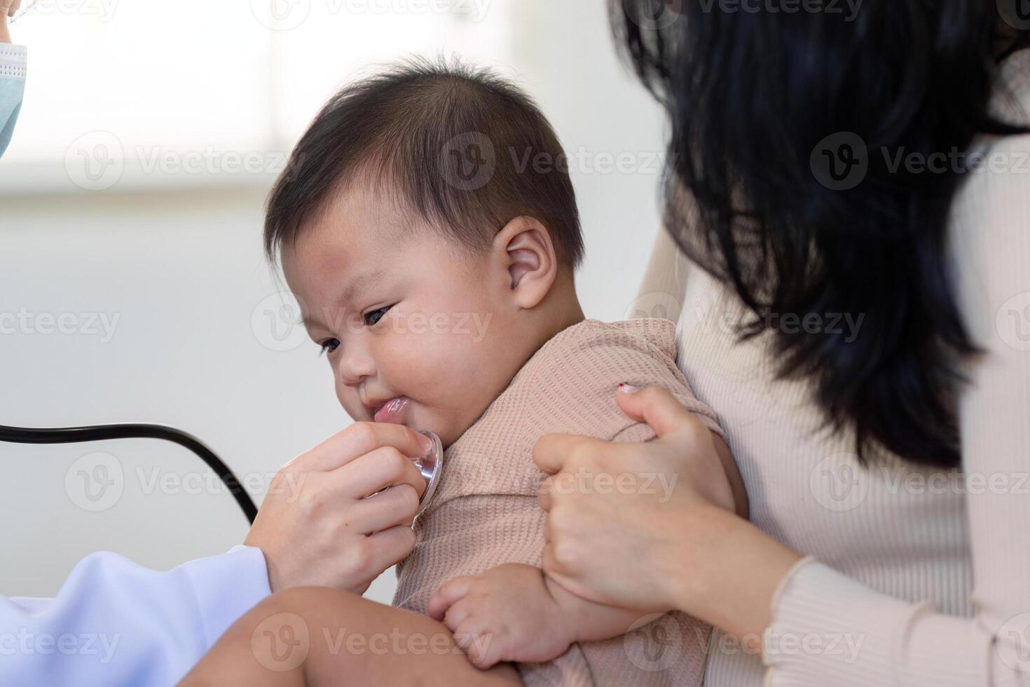 Pediatrician using stethoscope on baby during a checkup with attentive mother photo