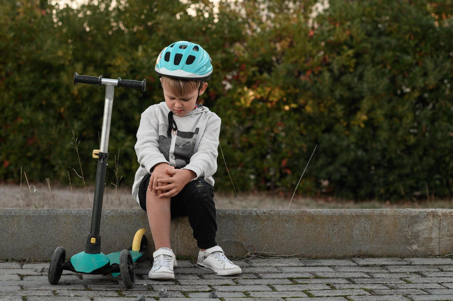 With a helmet on, the boy sits crying after scraping his knee. photo