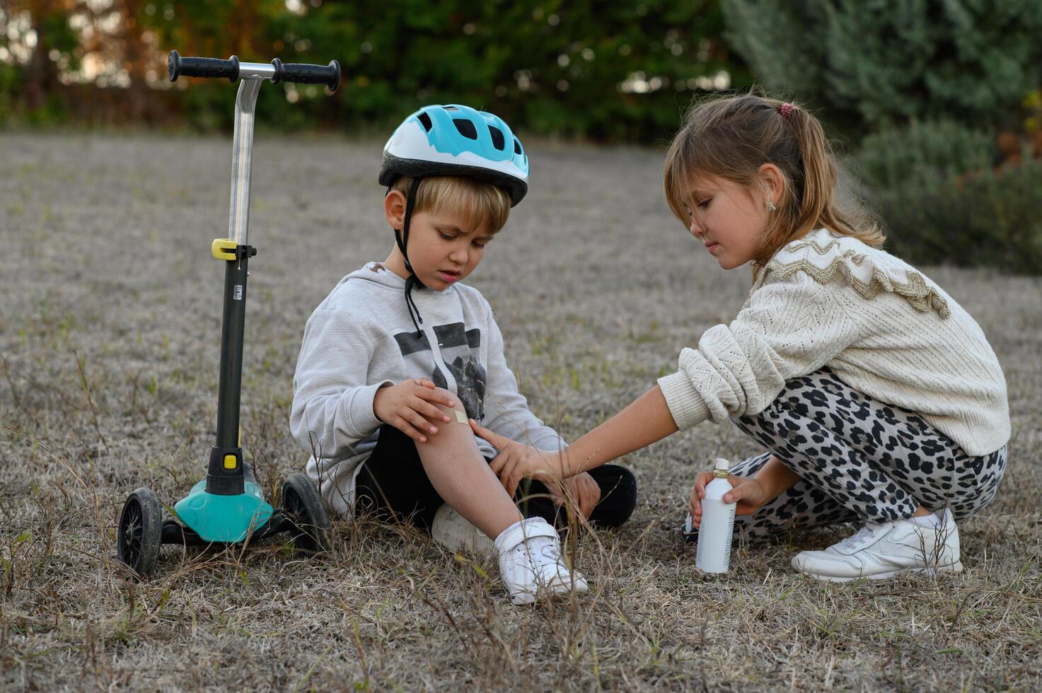 A girl comforts the boy beside his scooter, gently spraying antiseptic on his scraped knee as he cries. photo