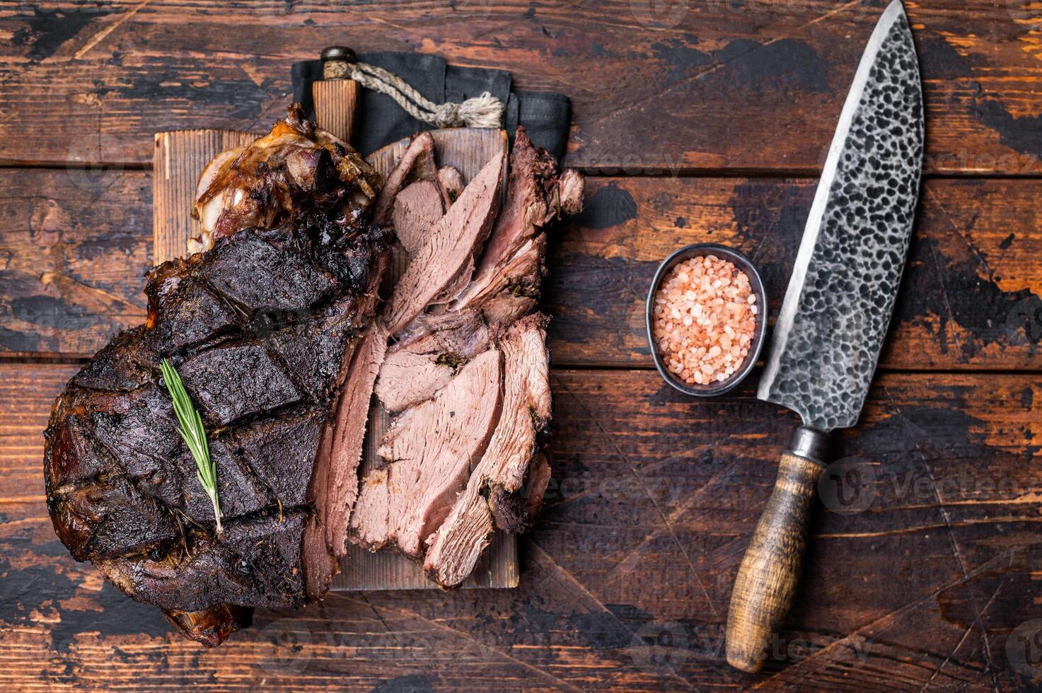 Slow ccoked sliced Venison leg, roasted game meat of deer on a board with herbs. wooden background. top view photo