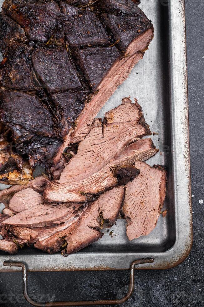 Roast Venison leg, baked meat of roe deer with bone on a tray with herbs. black background. top view photo