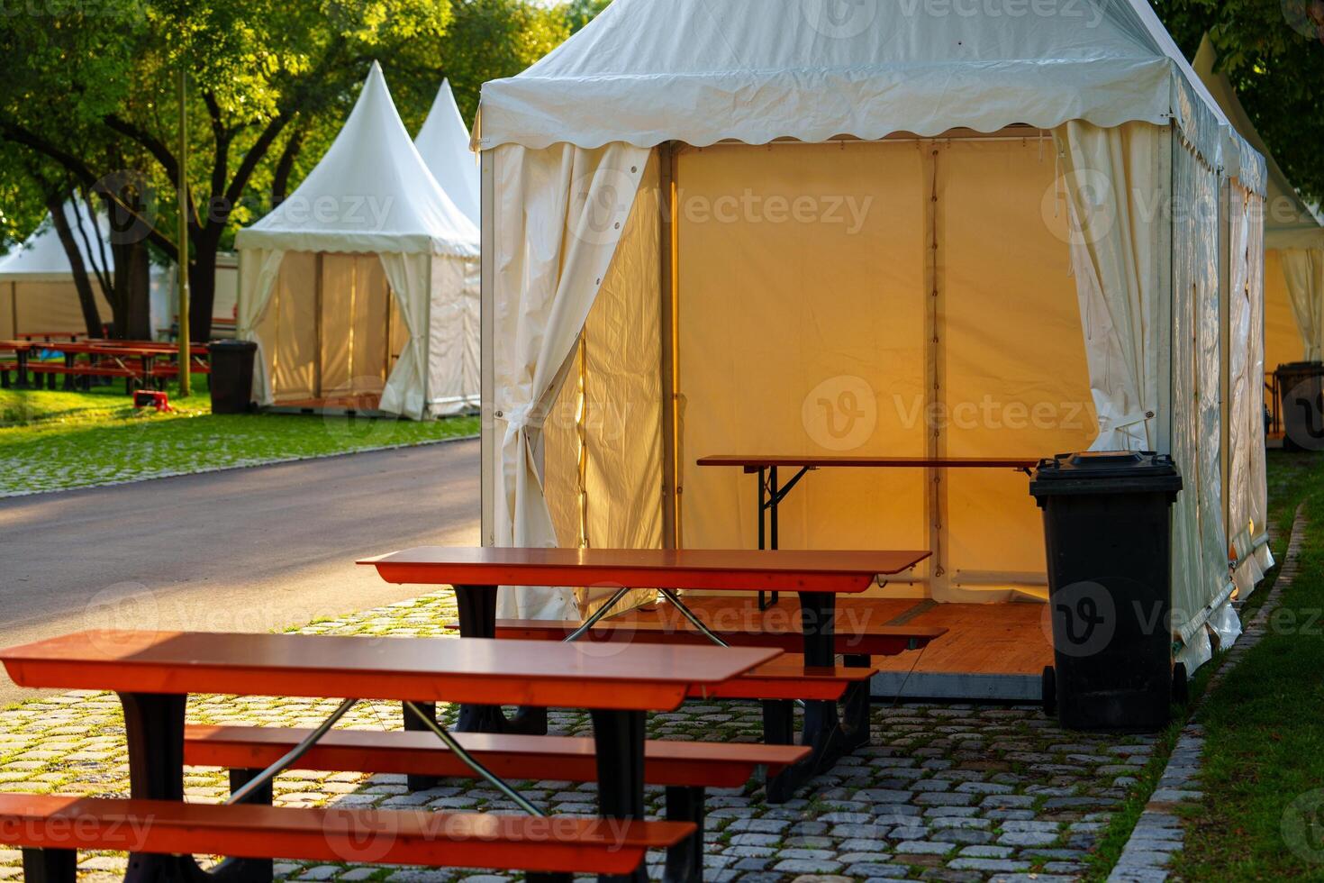 White party tent with red benches and tables outside on a sunny day. photo