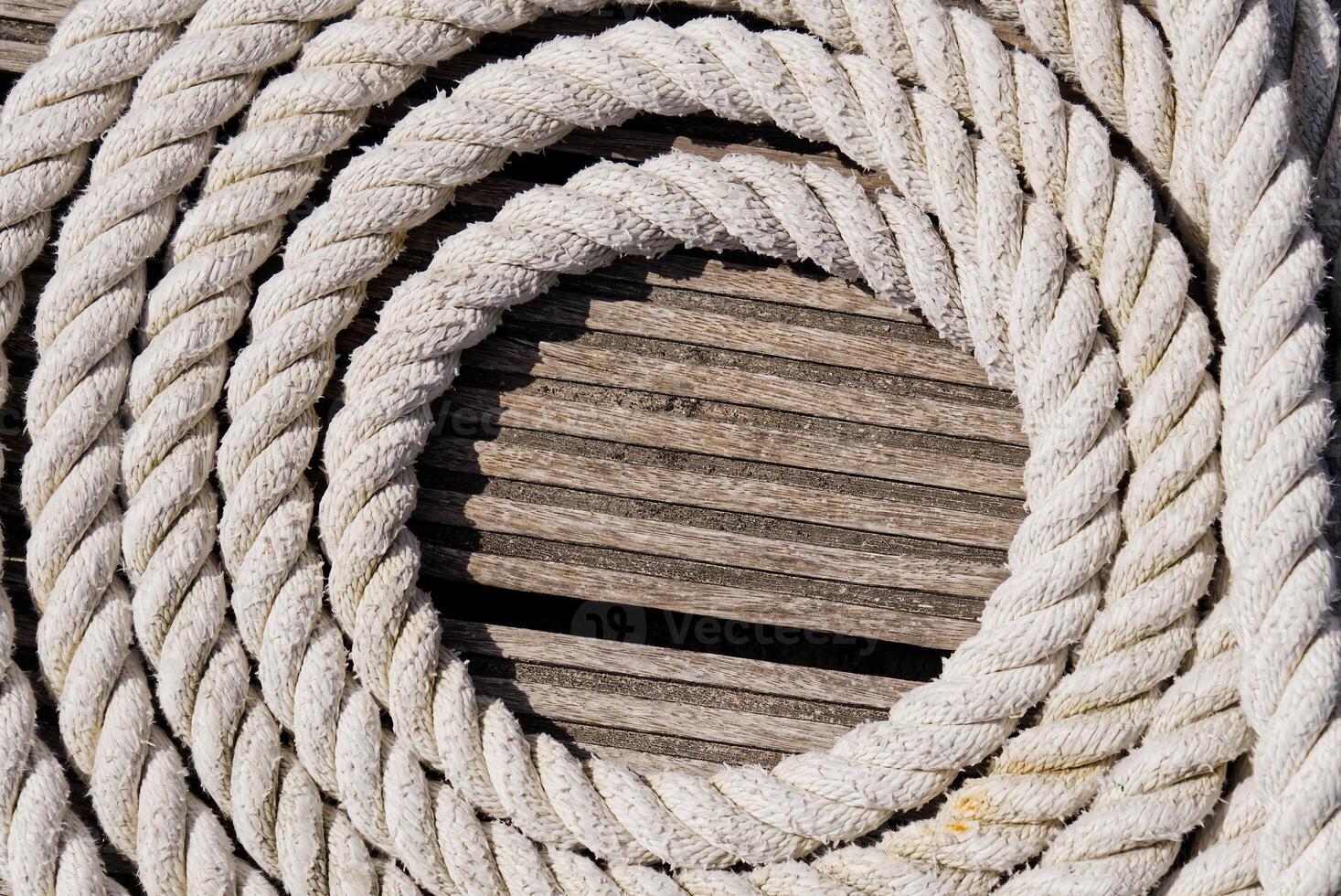 Thick White Rope Coiled Neatly on a Dark Wooden Dock for Nautical Activities and Boat Securing photo