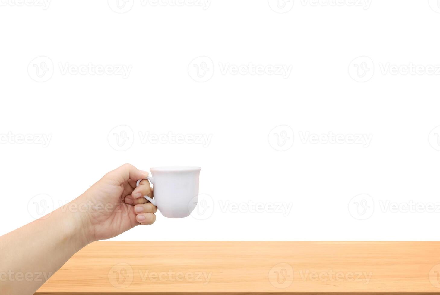 One hand holding a white ceramic coffee cup on a wooden table isolated on white background. photo