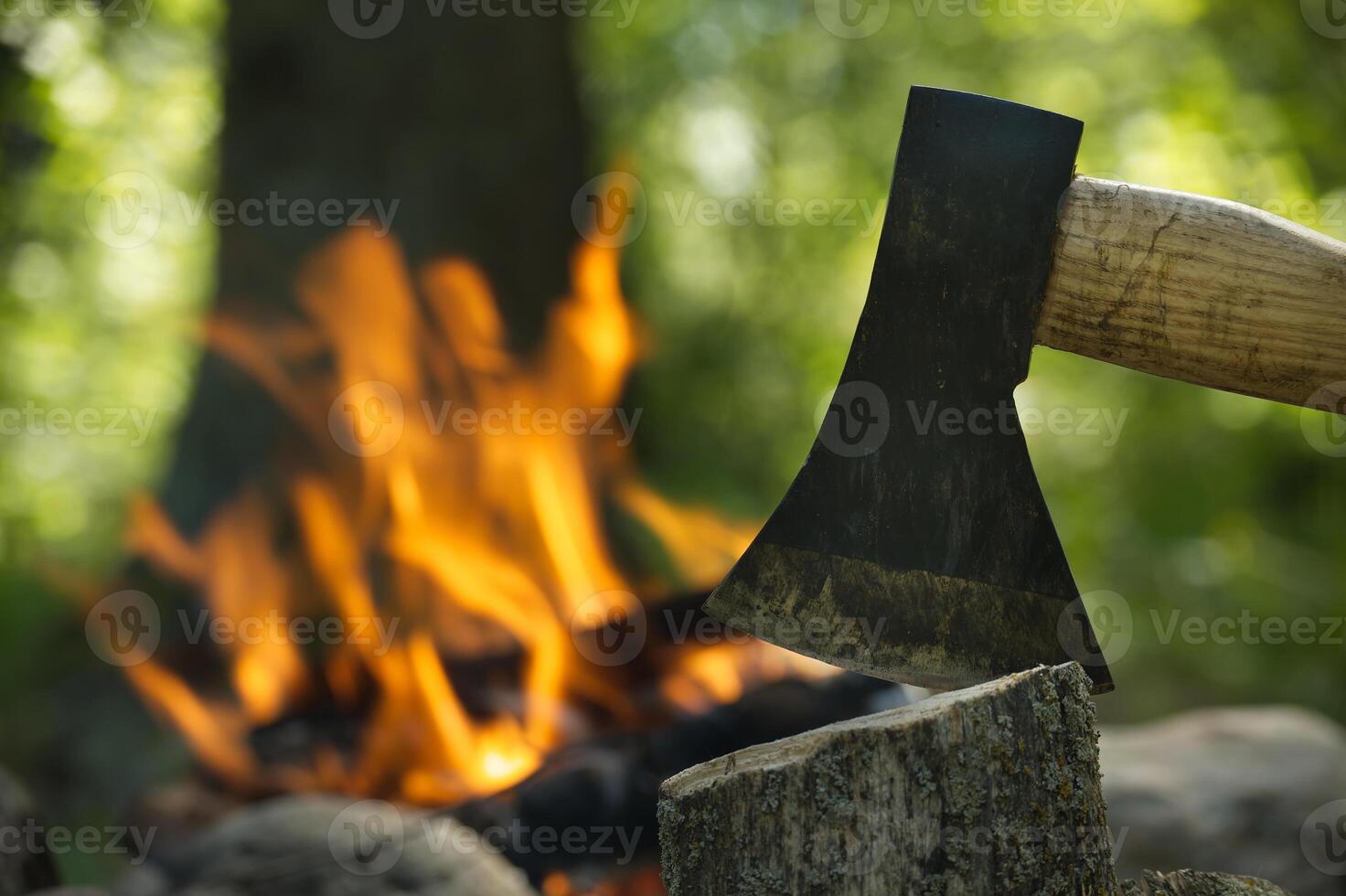 Axe splitting firewood in front of bonfire in forest photo