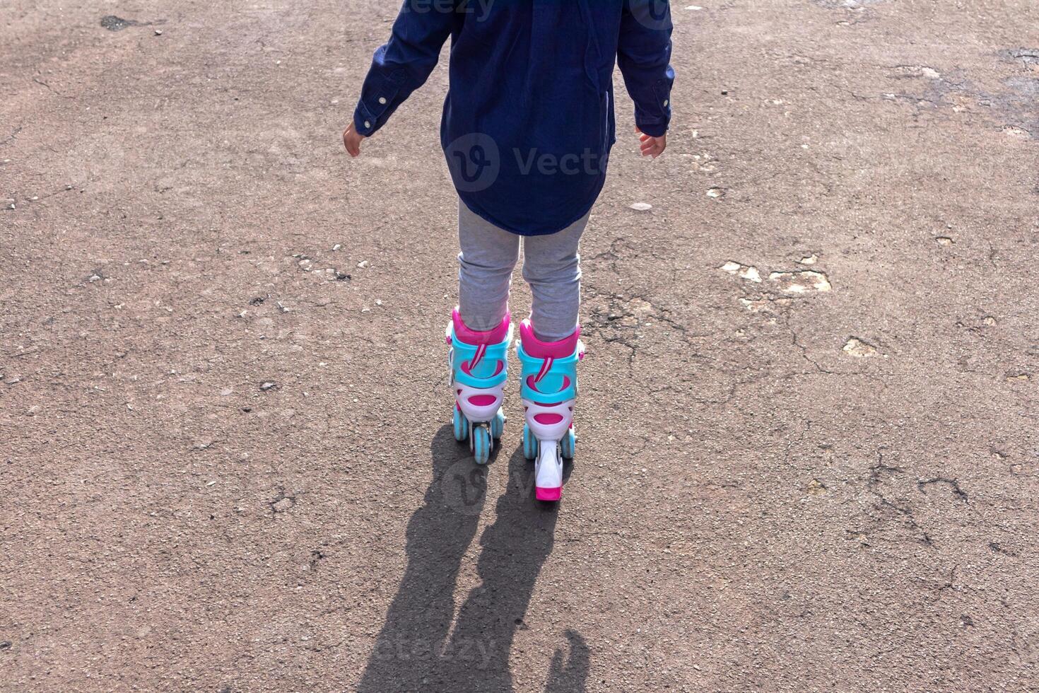 Back view of a little girl playing roller skates on the asphalt road photo