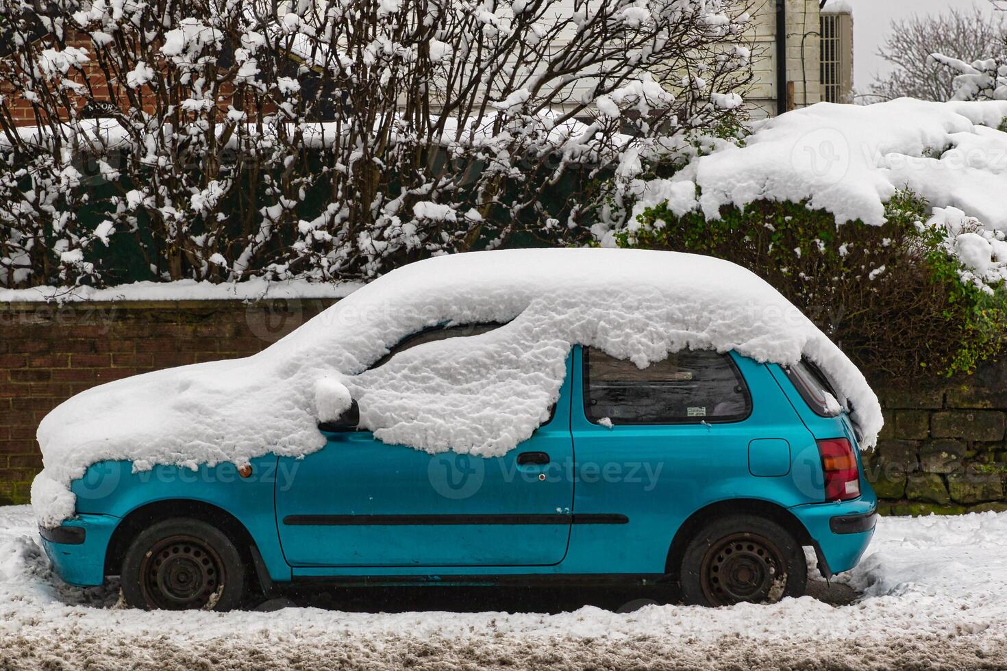 Snow-Covered Teal Hatchback Parked on Snowy Street in Harrogate, UK. photo