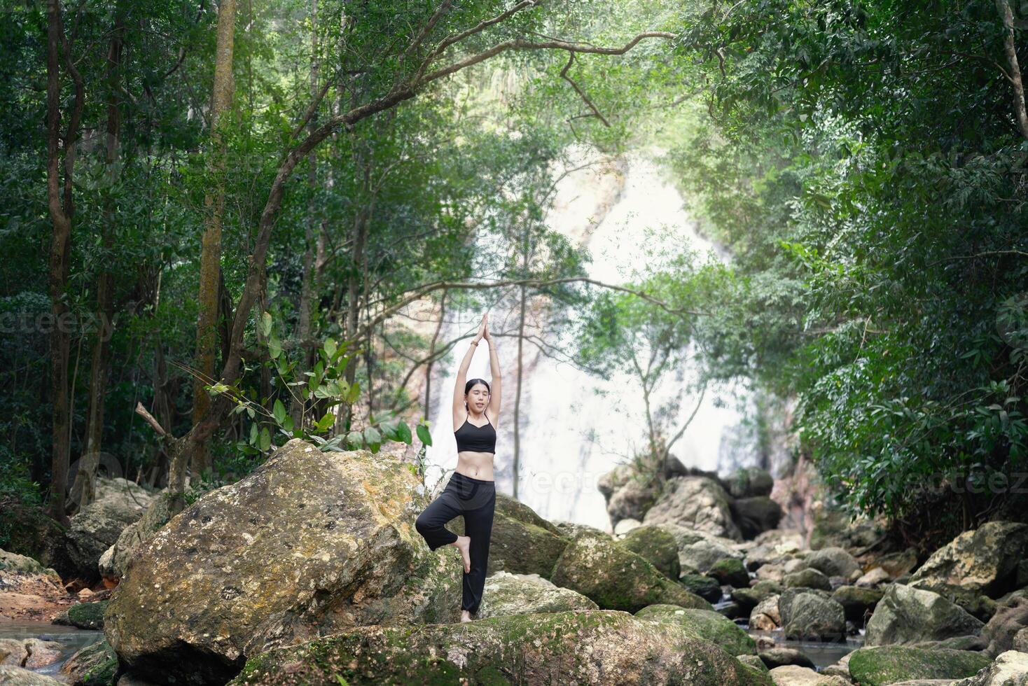 A woman meditating with a waterfall surrounded by nature, looking relaxed and stress-relieving photo