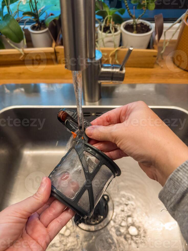 Hands cleaning a coffee machine filter under running water in kitchen sink. High quality photo