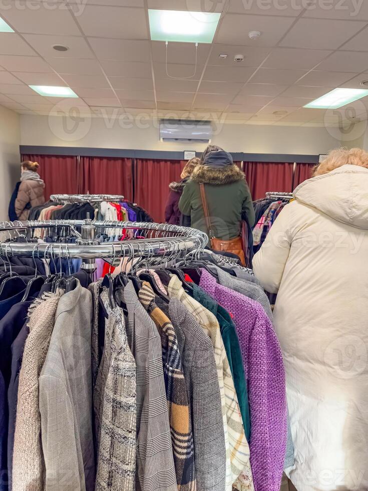 Thrift store shoppers browse racks of clothing. High quality photo