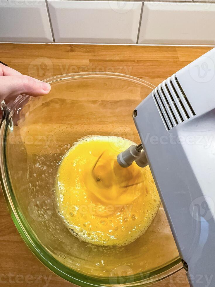 hand holds a mixing bowl while an electric mixer whips egg yolks in kitchen . High quality photo