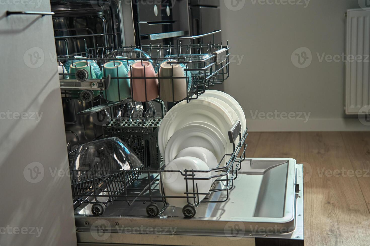 Open dishwasher in kitchen loaded clean crockery items, including white plates, bowls and cups ready for unloading. Modern home appliance photo