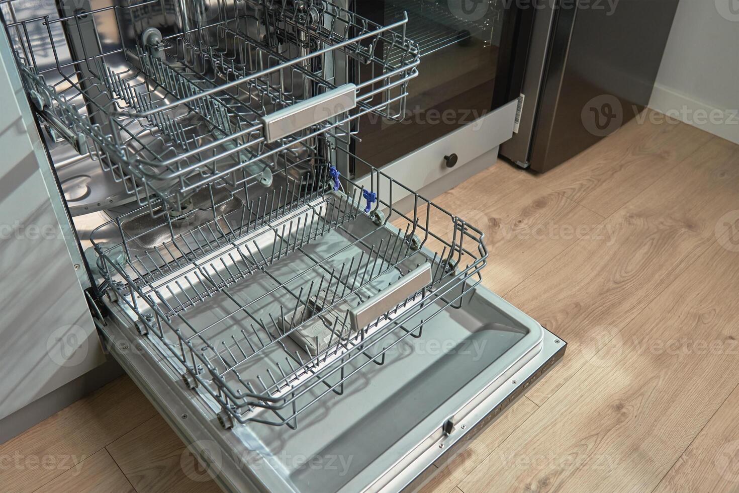 Open empty dishwasher with empty racks and extended basket in modern kitchen ready for loading. Home appliance photo