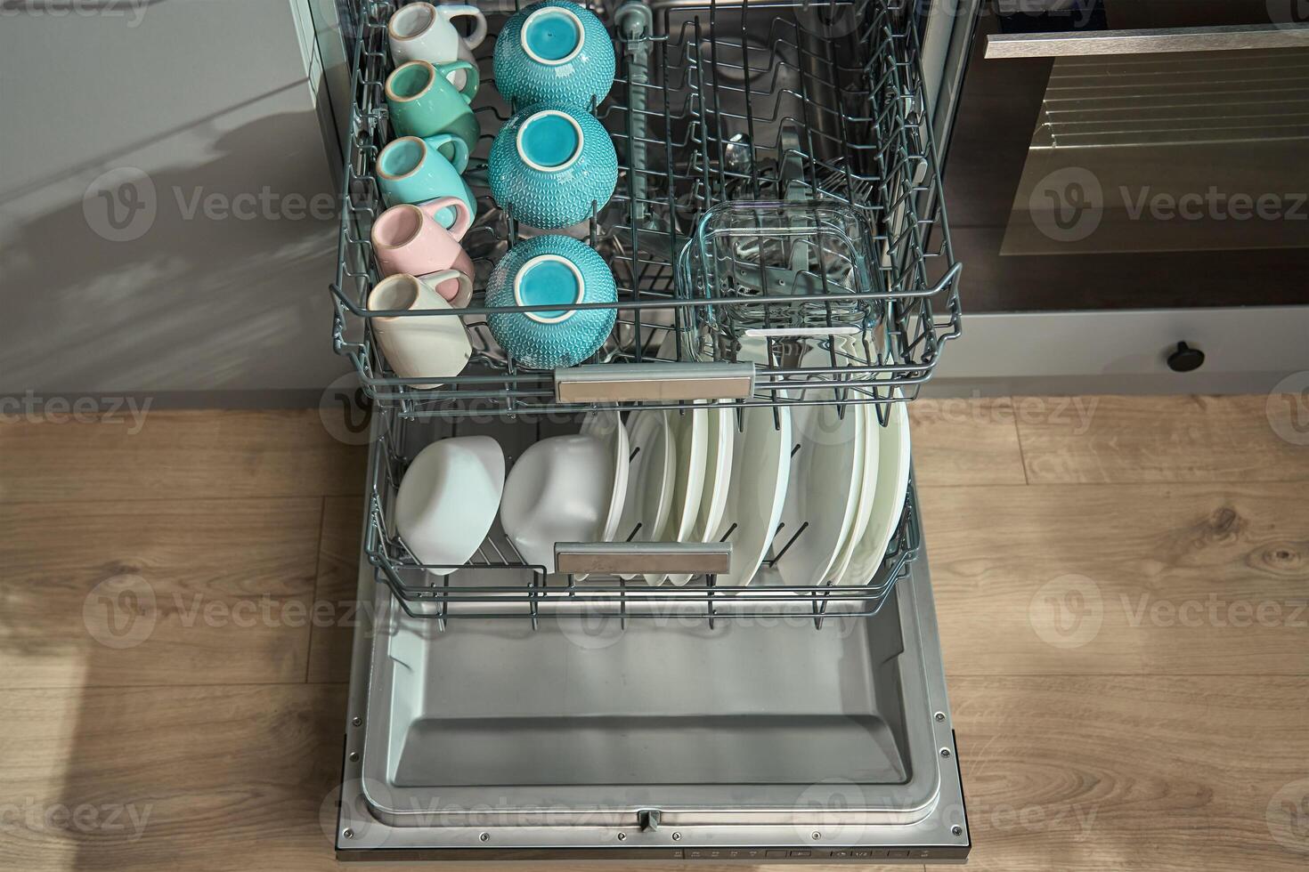 Open dishwasher in kitchen loaded clean crockery items, including white plates, bowls and cups ready for unloading. Modern home appliance photo