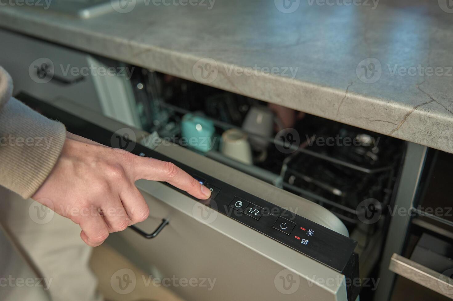 Hand pressing start button on dishwasher control panel with open door. Woman using modern home appliance, choosing automatic program on built in dishwasher for cleaning dirty dishes photo