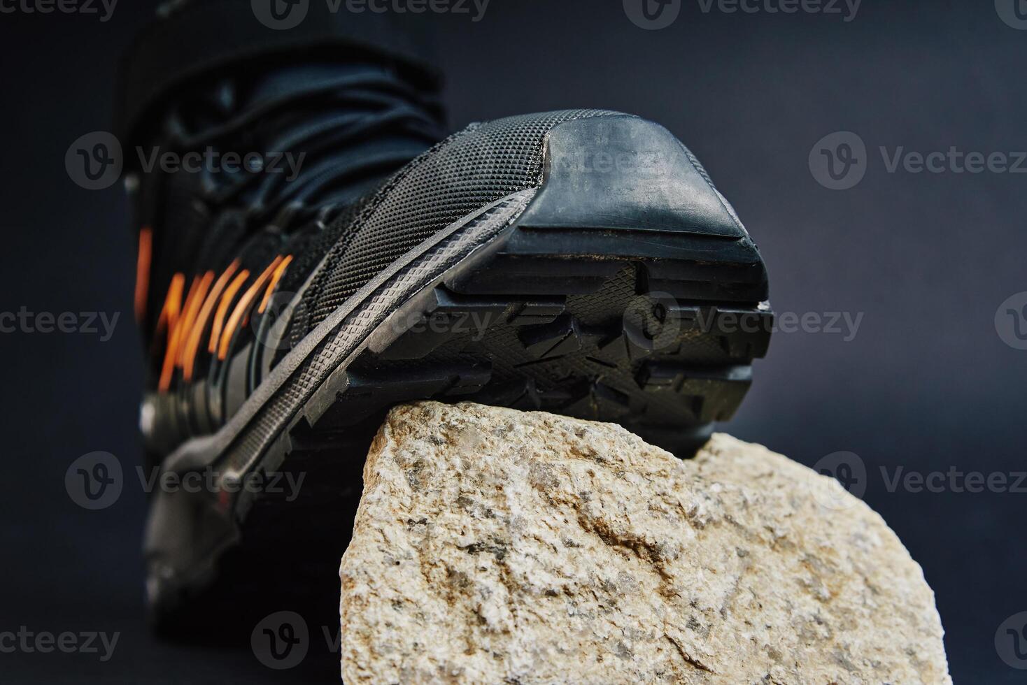 Close-up of waterproof black hiking shoe with orange details on small rock. Rugged trekking boot on dark background. Footwear for exploration and outdoor activities photo