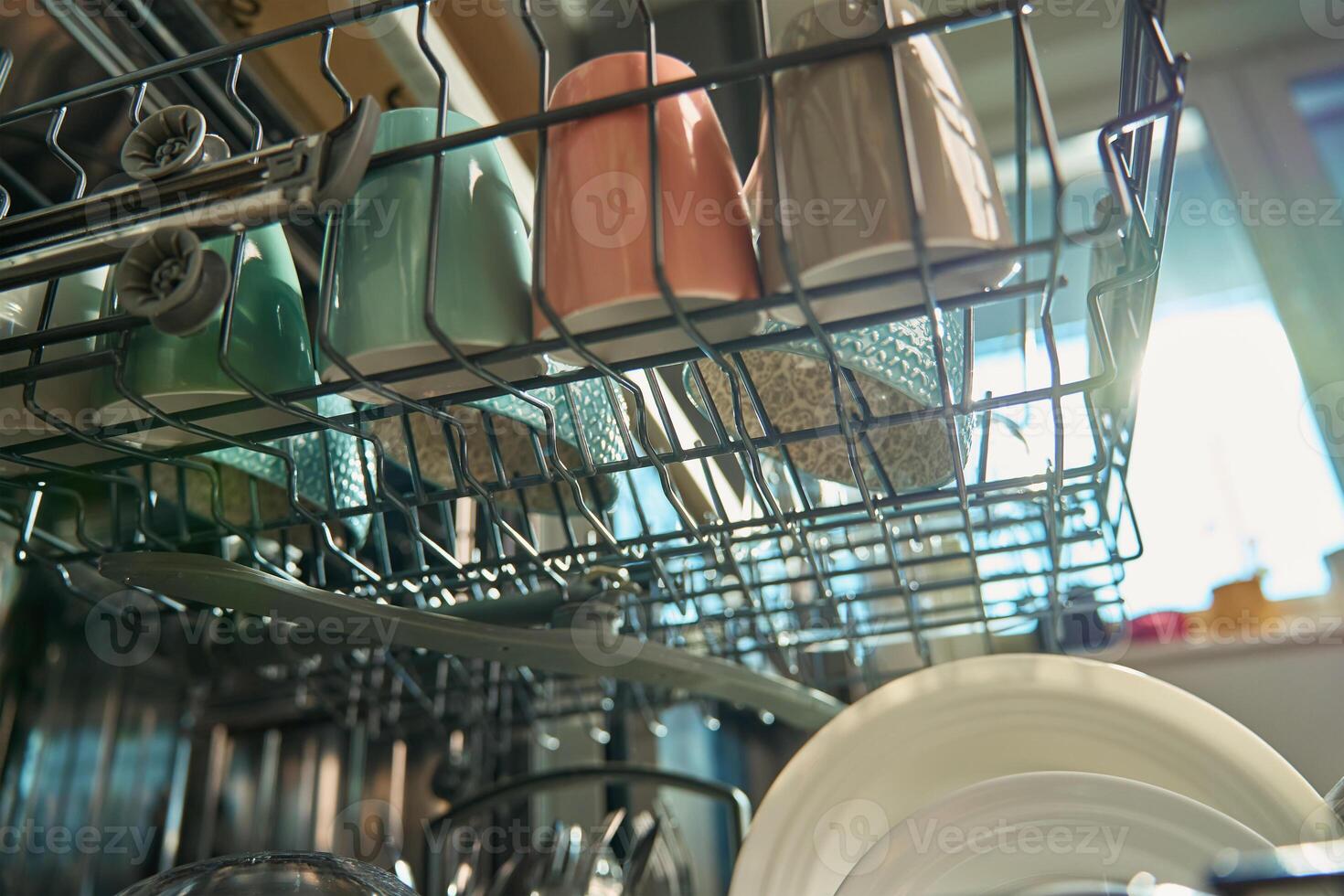 Open dishwasher in kitchen loaded clean crockery items, including white plates, bowls and cups ready for unloading. Modern home appliance photo