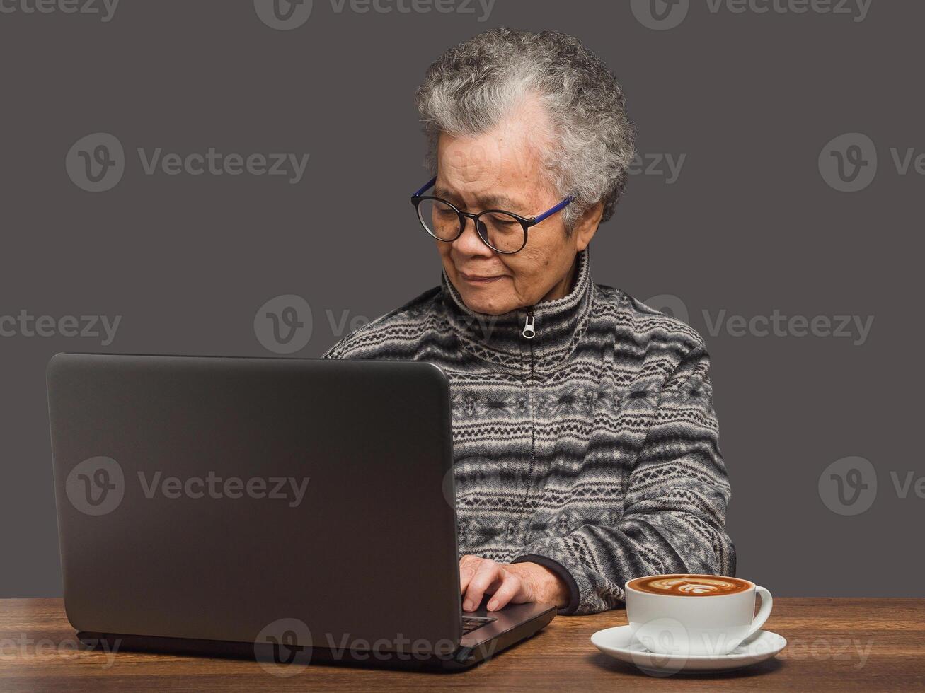 An elderly Asian woman with short grey hair uses a laptop to search for data from the internet while sitting at the table photo
