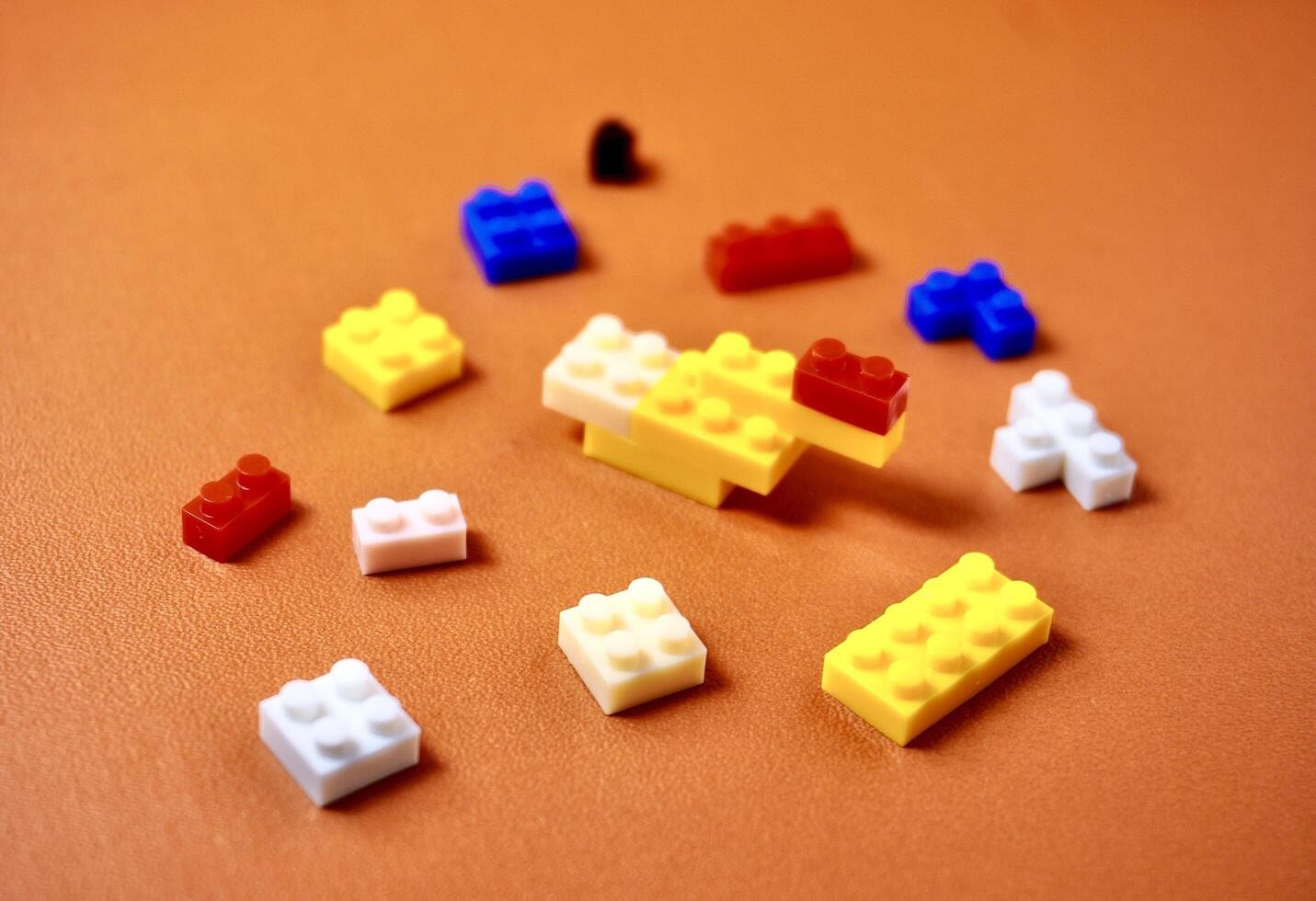 Yellow, blue, red, pink, and white colored bricks toys building game pieces isolated on horizontal orange brown colored background. photo
