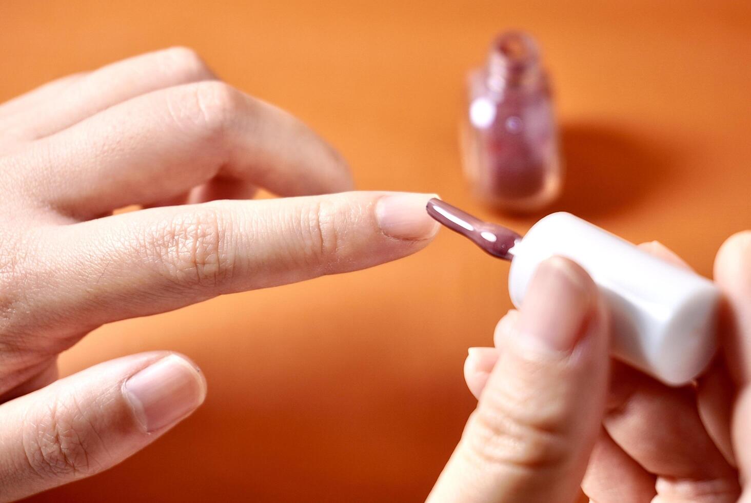 Hand applying nail polish on fingernail isolated on horizontal orange brown terracotta colored background. photo