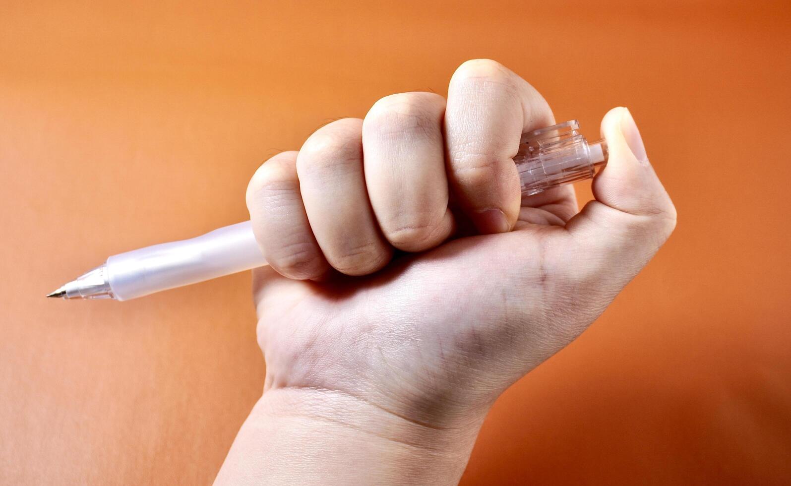 Hand holding and clicking mechanical pencil isolated on horizontal orange brown terracotta colored background. photo
