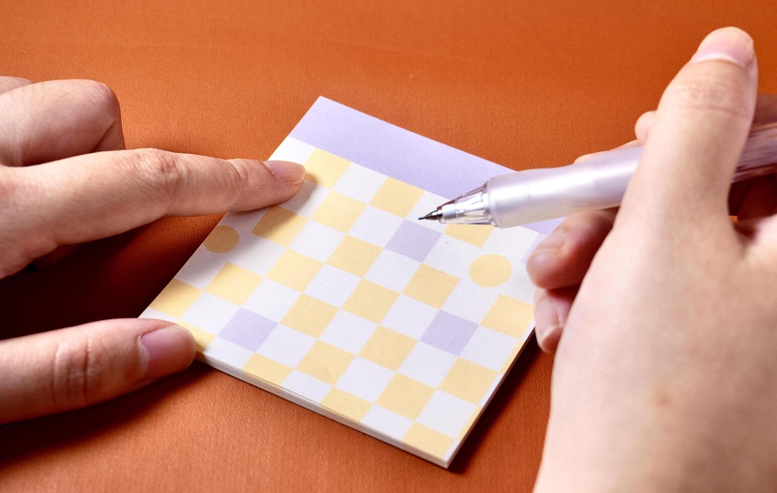 Hand holding mechanical pencil with square note memo paper on the back isolated on horizontal orange brown terracotta colored background. photo