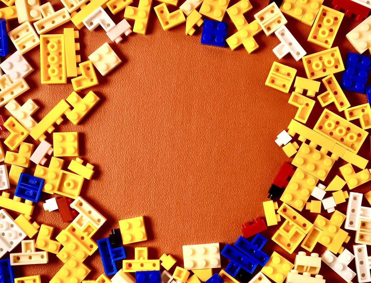 Yellow, blue, red, and white colored bricks toys building game pieces isolated on horizontal orange brown colored background with round copy space from top angle view. photo